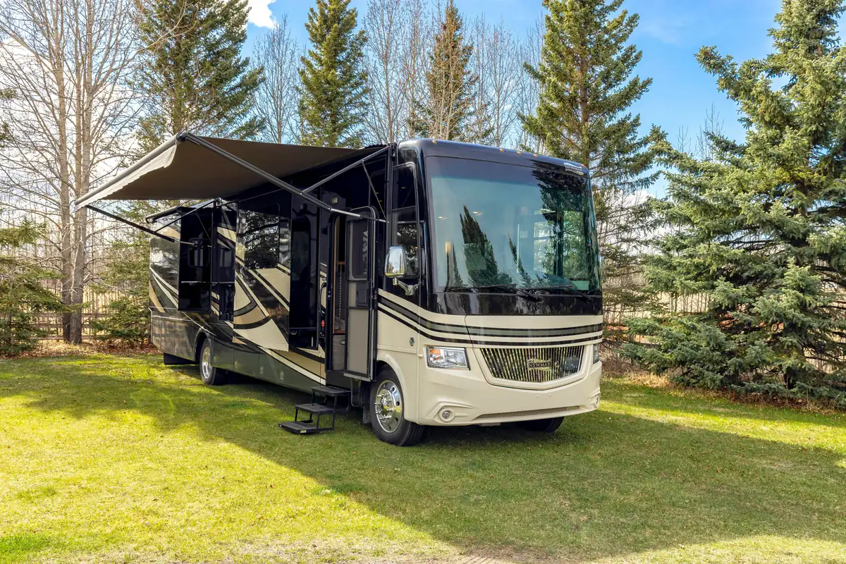 Class A motorhome with its awning and slide-outs extended, parked on grass among pine trees