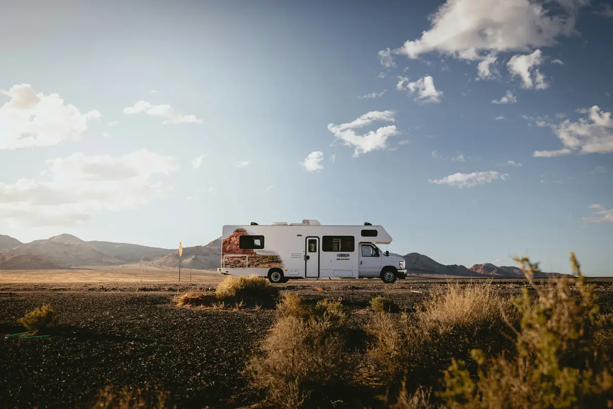 Class C motorhome parked on a desert road with mountains in the background