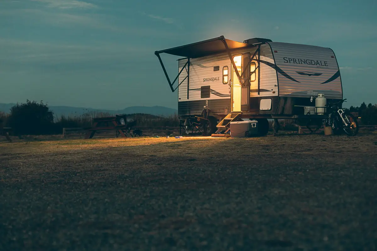 Travel trailer at dusk with its awning out and the door light on at a campsite